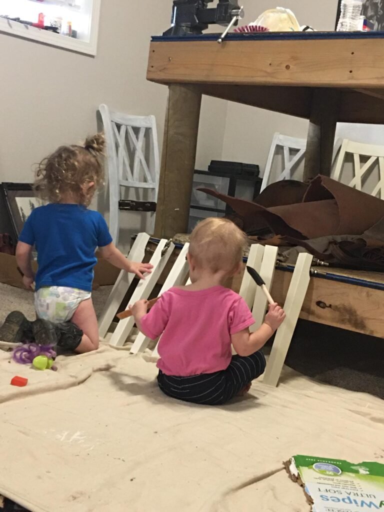 two toddler girls helping paint chair and table legs